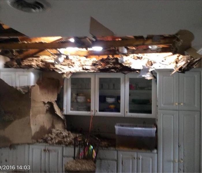 White kitchen with hole in the ceiling and large debris all over everything