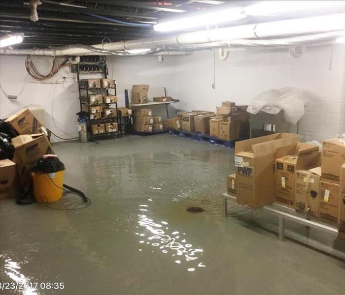 Gray and white basement with inches of water on the floor and boxes on shelving